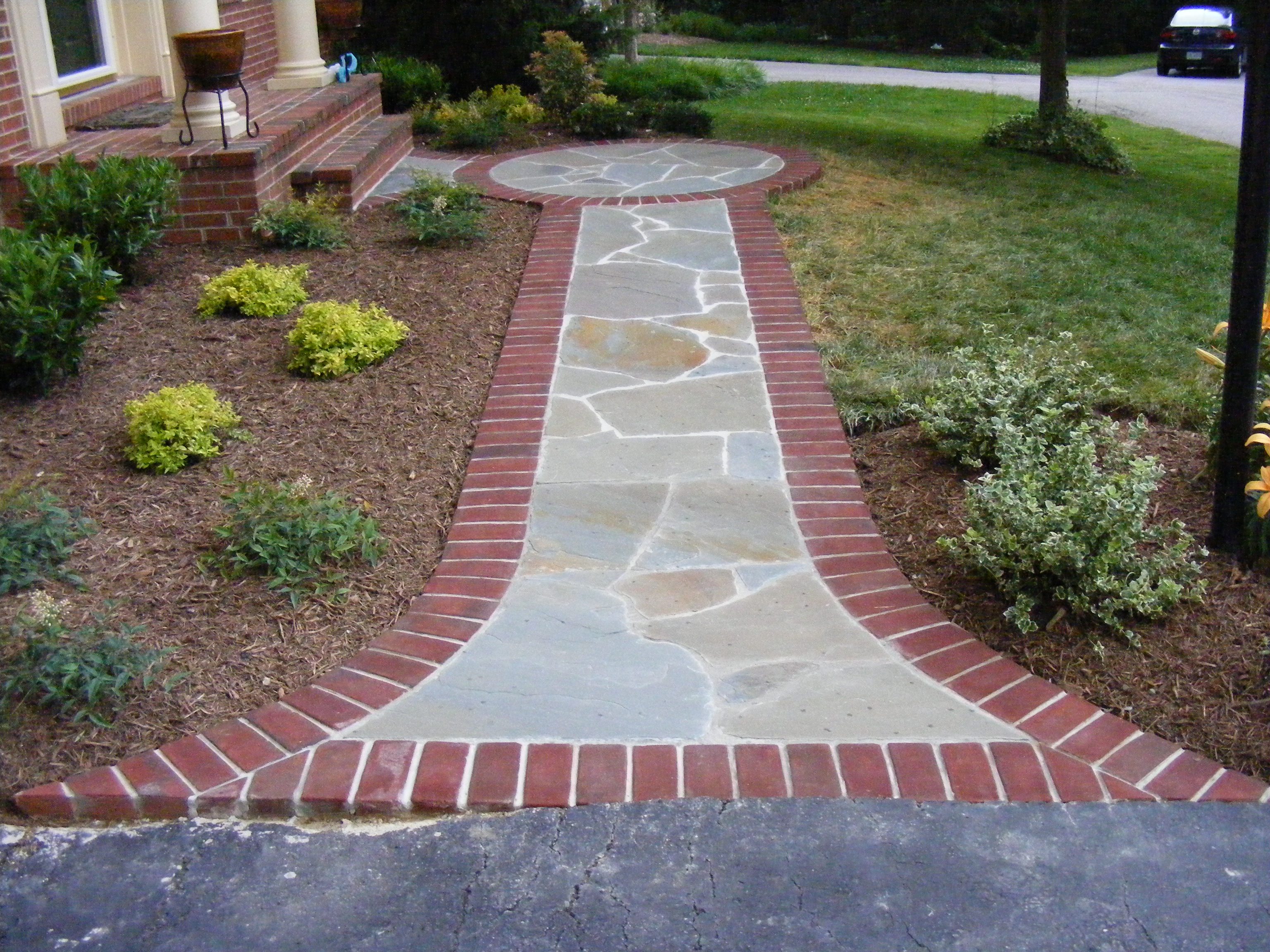 A walkway with brick and stone border in the middle of a yard.