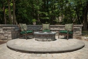 A fire pit with chairs and trees in the background.