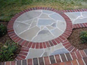 A circular stone patio with brick border and a circle design.