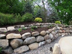 A stone wall with plants and trees in the background.